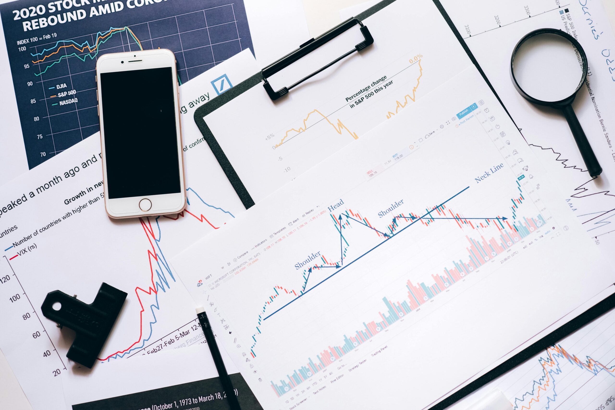 Stock market analysis setup with charts, phone, magnifier, and clipboards.